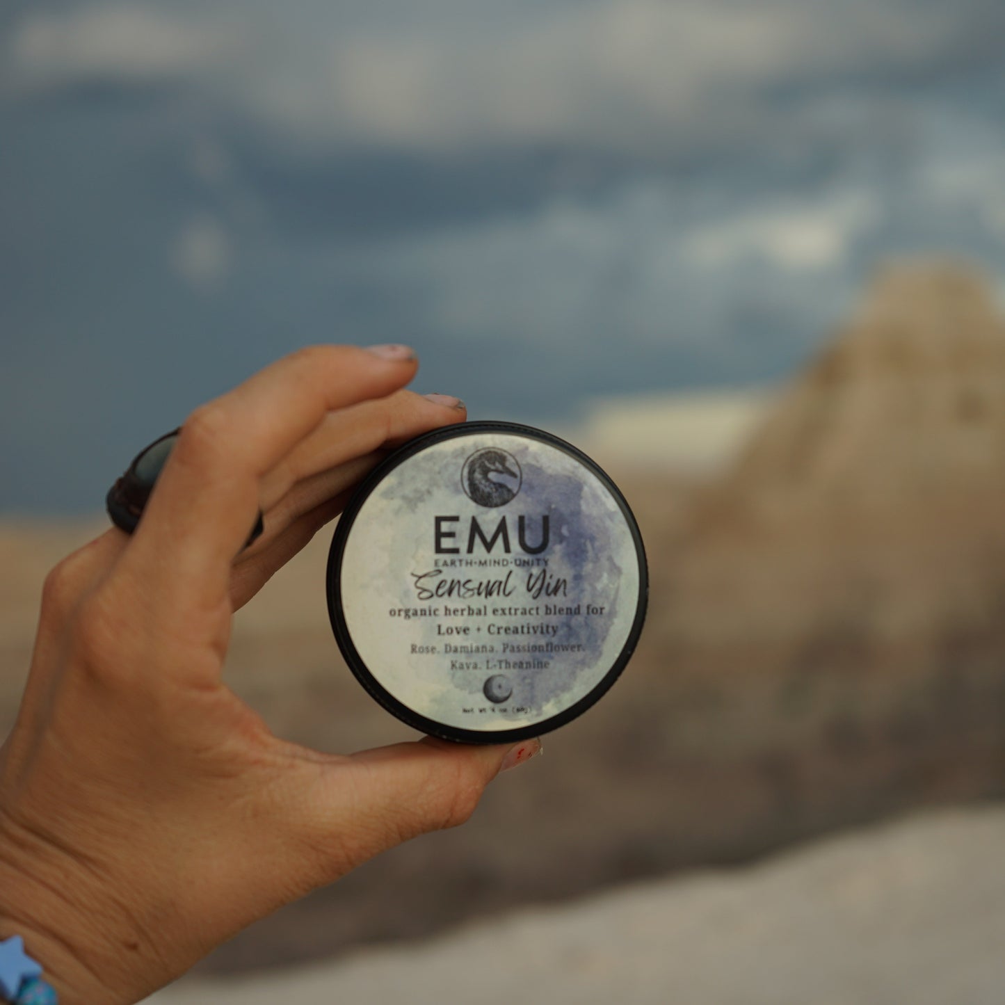 Hand holding a container labeled 'EMU' against a blurred natural background